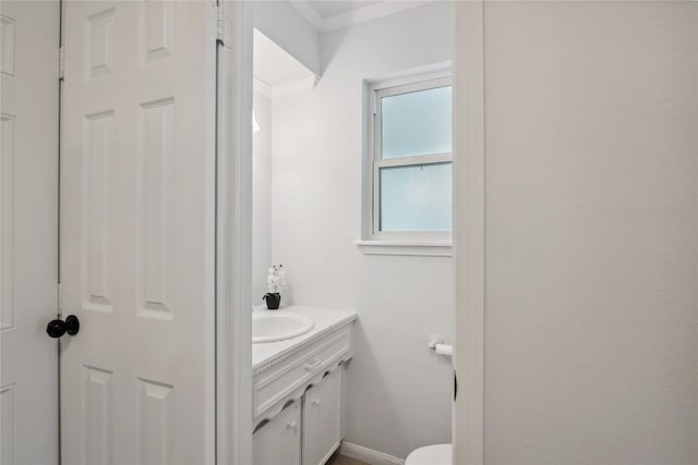 half bath featuring toilet, crown molding, vanity, and baseboards