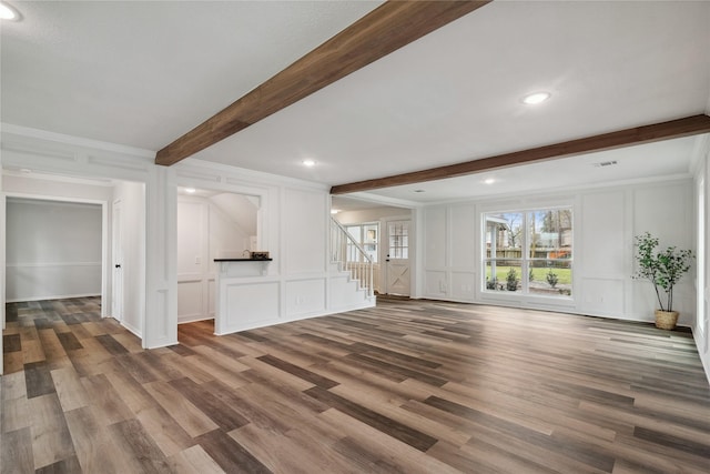 unfurnished living room featuring a decorative wall, stairway, beamed ceiling, and wood finished floors