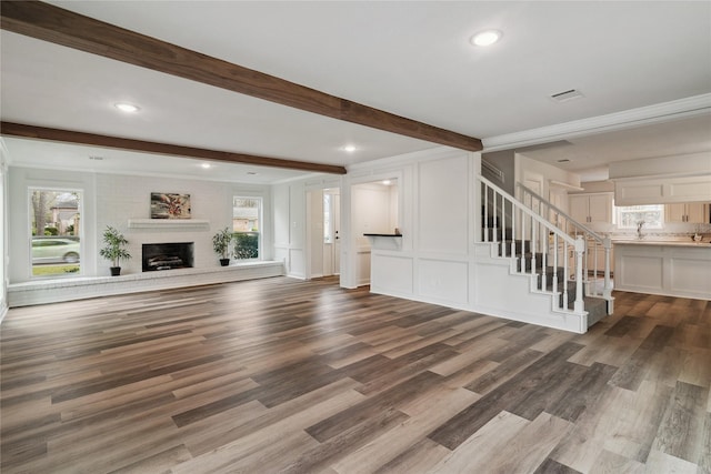 unfurnished living room featuring beam ceiling, visible vents, a brick fireplace, wood finished floors, and stairs