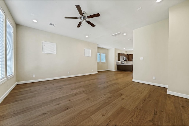 unfurnished living room with visible vents, plenty of natural light, baseboards, and wood finished floors