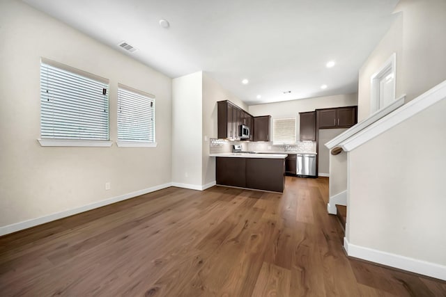 kitchen with tasteful backsplash, light countertops, stainless steel microwave, dark brown cabinetry, and baseboards