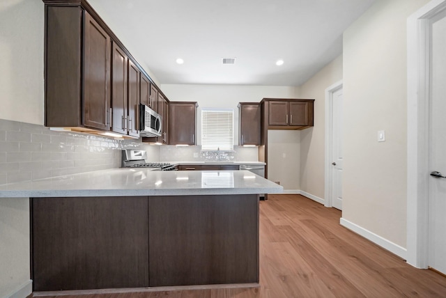 kitchen with stainless steel appliances, tasteful backsplash, visible vents, dark brown cabinets, and a peninsula