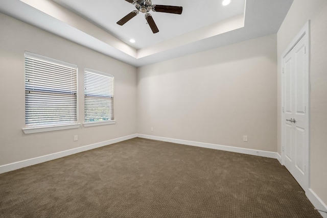 spare room with dark colored carpet, a raised ceiling, baseboards, and recessed lighting