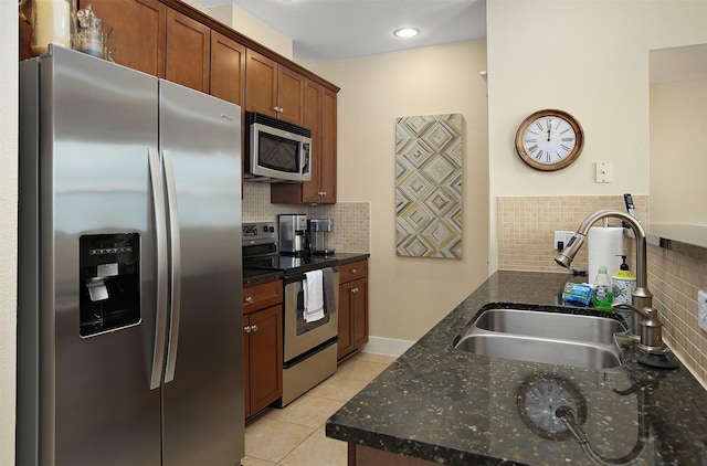 kitchen featuring tasteful backsplash, dark stone counters, light tile patterned floors, appliances with stainless steel finishes, and a sink