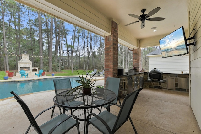 view of patio with ceiling fan, exterior kitchen, an outdoor stone fireplace, outdoor dining area, and area for grilling