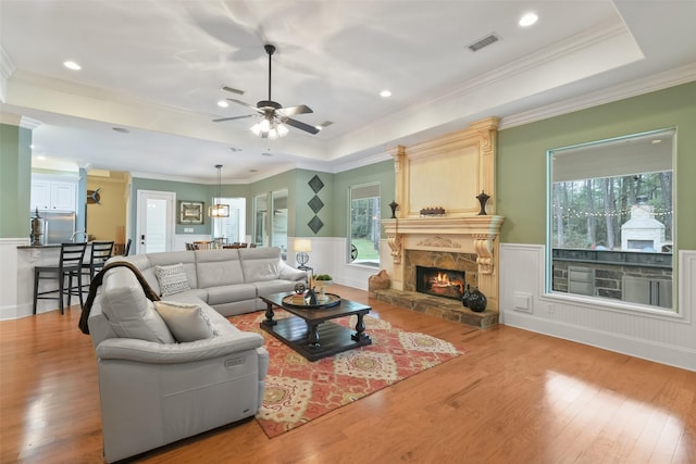 living area with visible vents, a healthy amount of sunlight, a tray ceiling, and wood finished floors