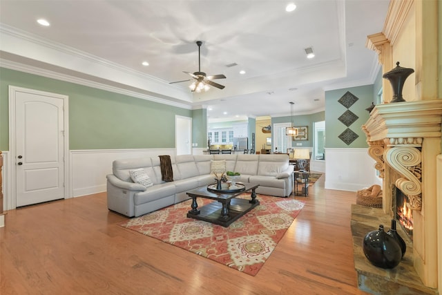 living room featuring a raised ceiling, a lit fireplace, wood finished floors, and wainscoting