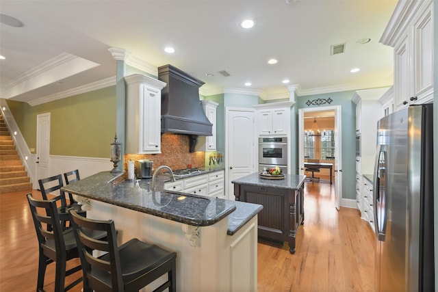 kitchen featuring visible vents, custom range hood, a peninsula, light wood-style floors, and stainless steel appliances