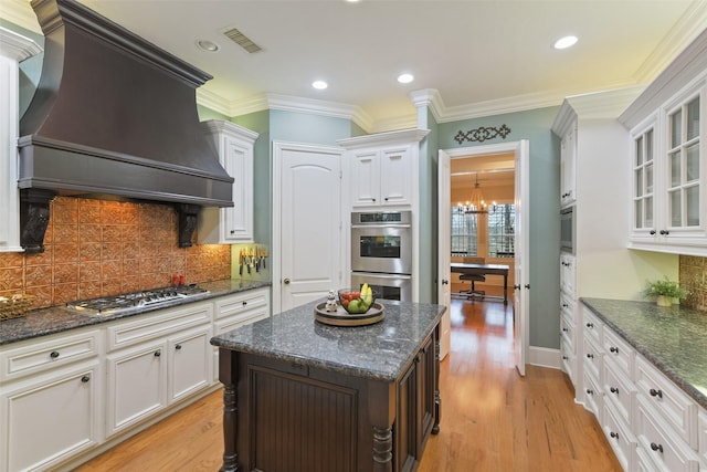 kitchen with glass insert cabinets, light wood-type flooring, custom range hood, decorative backsplash, and appliances with stainless steel finishes