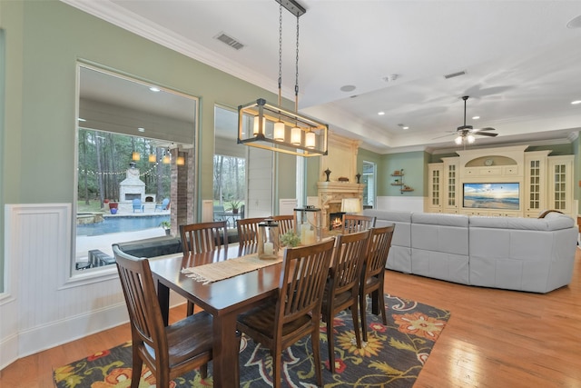 dining space featuring light wood-style flooring, ornamental molding, visible vents, and a lit fireplace