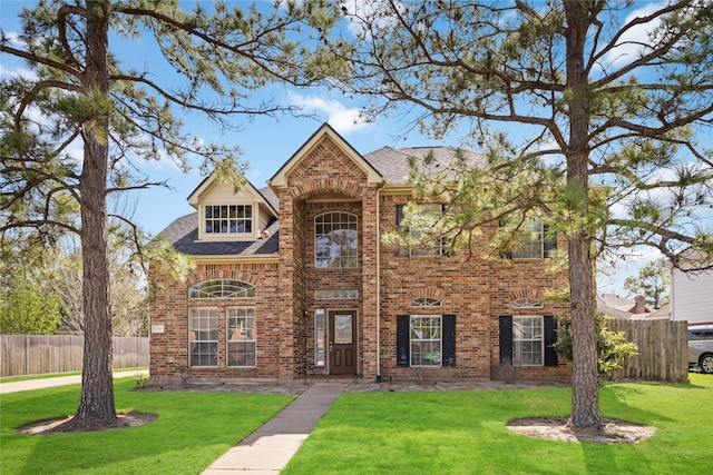 traditional-style house featuring a front yard, brick siding, fence, and roof with shingles