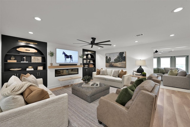 living area featuring light wood-style floors, visible vents, built in features, and recessed lighting