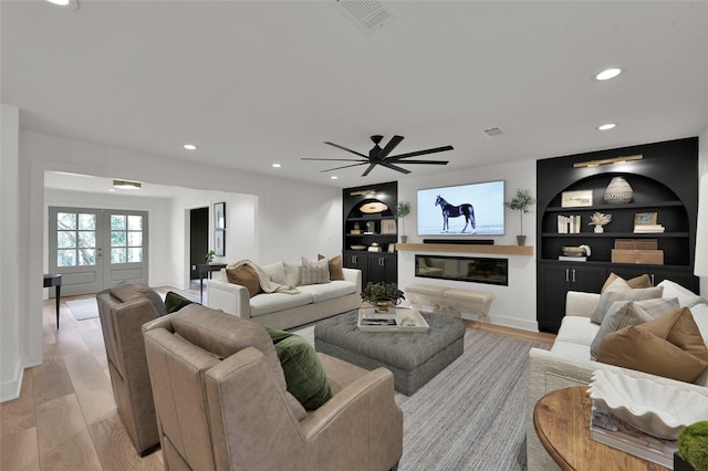 living area featuring built in features, light wood-type flooring, visible vents, and a glass covered fireplace