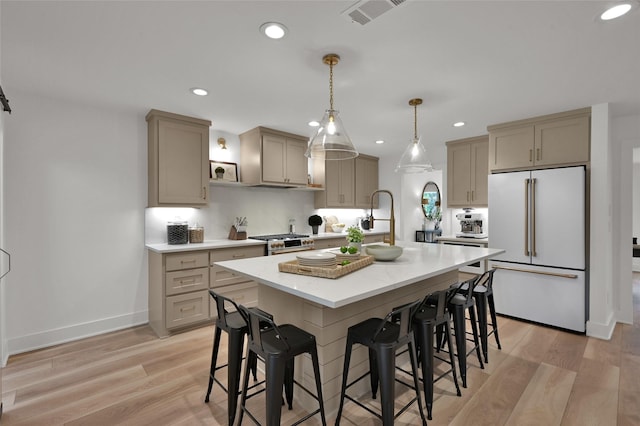 kitchen featuring premium appliances, visible vents, a kitchen breakfast bar, light wood finished floors, and a center island with sink