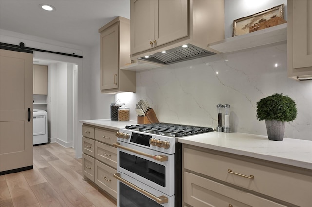 kitchen with range with two ovens, a barn door, light wood-style flooring, tasteful backsplash, and washer / dryer