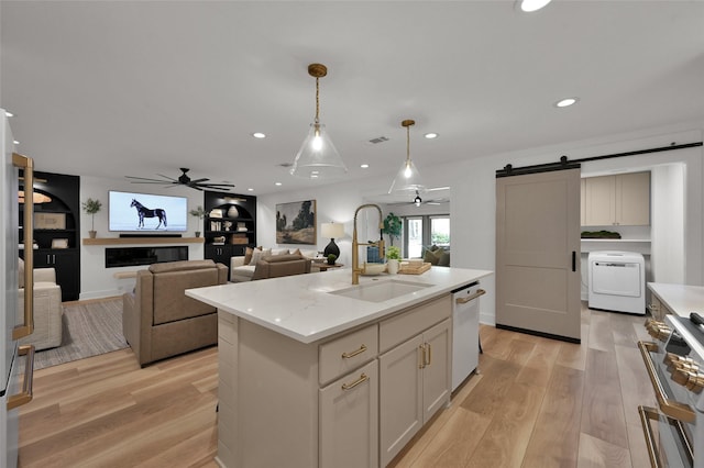 kitchen featuring a barn door, white dishwasher, light wood-style flooring, a sink, and washer / dryer