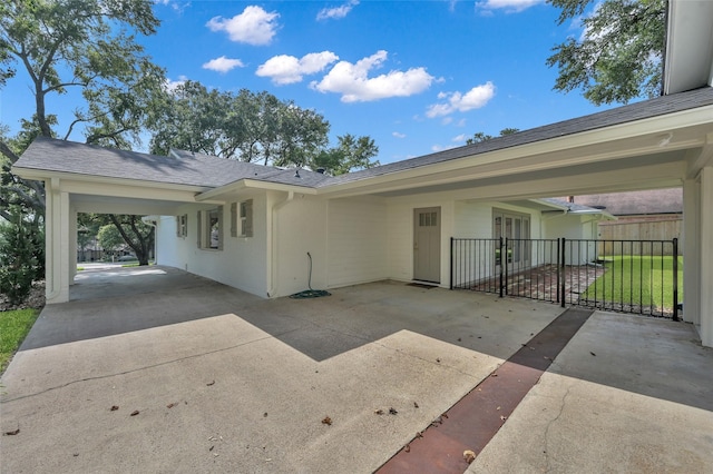 view of front facade featuring concrete driveway, a carport, roof with shingles, and fence