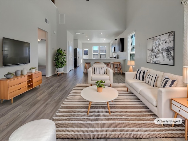 living area with wood finished floors, visible vents, a towering ceiling, and baseboards