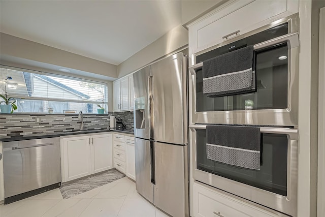 kitchen with a sink, white cabinetry, appliances with stainless steel finishes, backsplash, and dark countertops