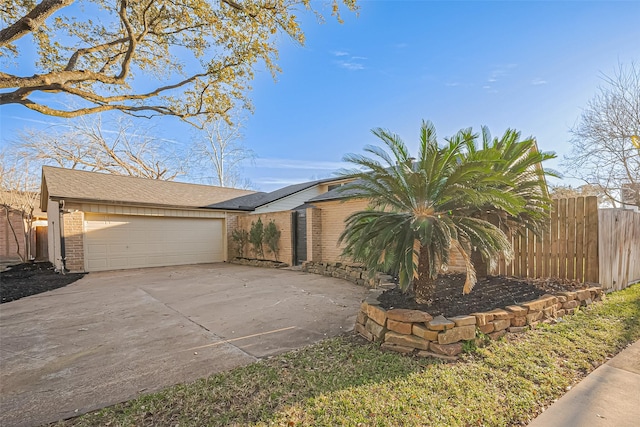 view of side of property with brick siding, driveway, an attached garage, and fence