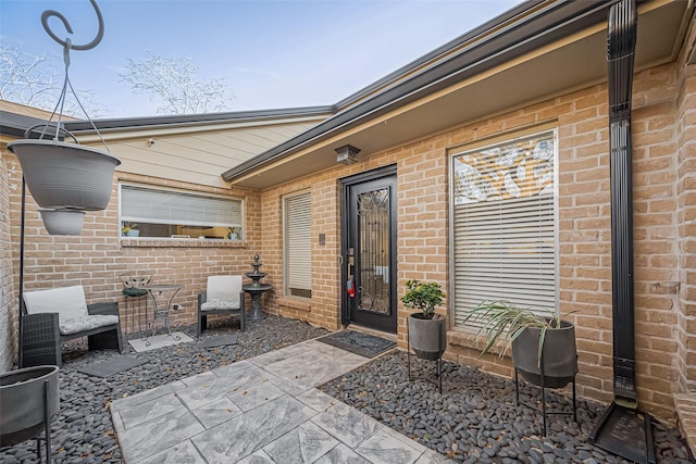 view of exterior entry featuring brick siding and a patio