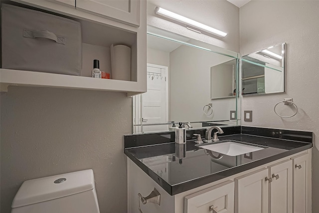 bathroom with a textured wall, vanity, and toilet