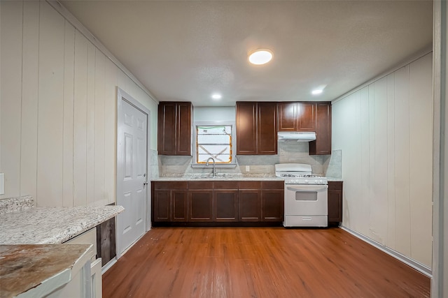 kitchen with white range with gas stovetop, backsplash, light wood-type flooring, under cabinet range hood, and a sink