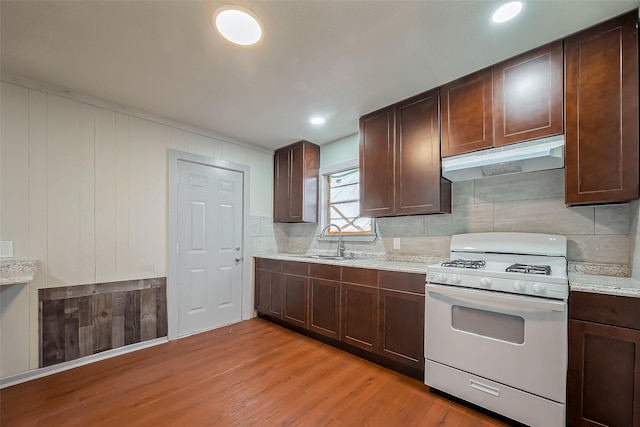 kitchen featuring under cabinet range hood, a sink, light wood-style floors, white gas range oven, and decorative backsplash