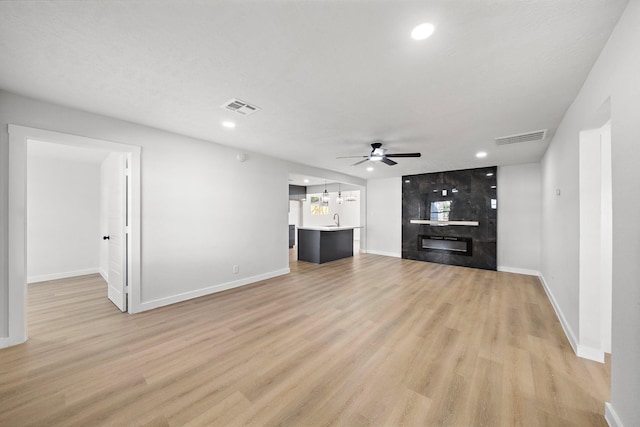 unfurnished living room with a ceiling fan, a fireplace, visible vents, and light wood-style floors