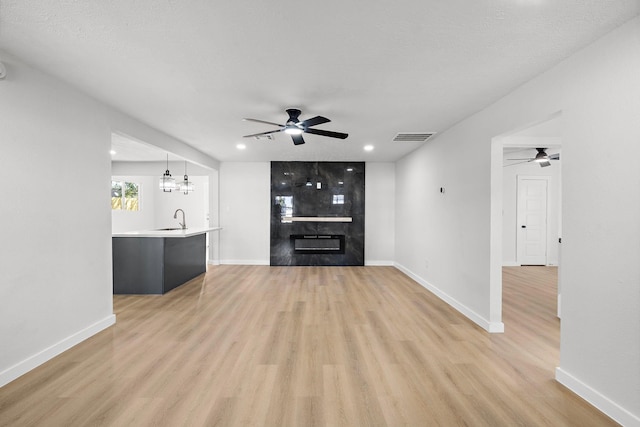 unfurnished living room featuring a large fireplace, light wood-style flooring, a sink, and visible vents