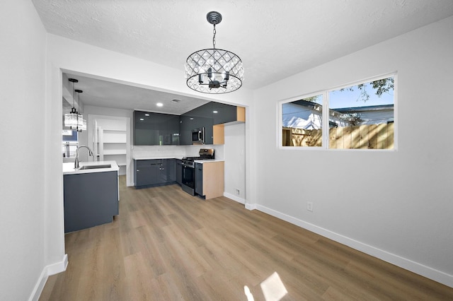 kitchen with appliances with stainless steel finishes, light countertops, light wood-style floors, a chandelier, and a sink