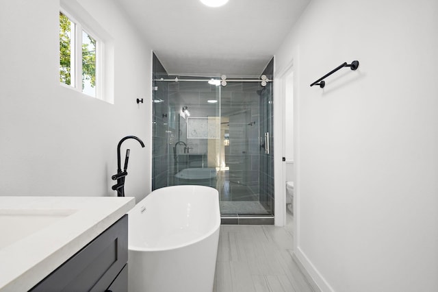 bathroom featuring toilet, vanity, baseboards, a freestanding bath, and a shower stall