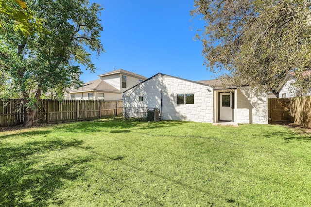 back of property with concrete block siding, a fenced backyard, and a lawn