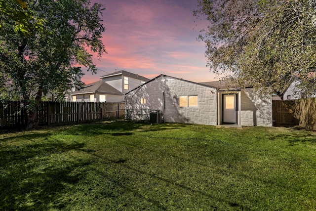 back of property at dusk with a yard, a fenced backyard, and concrete block siding