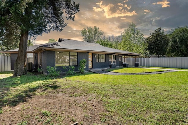 back of property at dusk featuring cooling unit, brick siding, fence, and a lawn