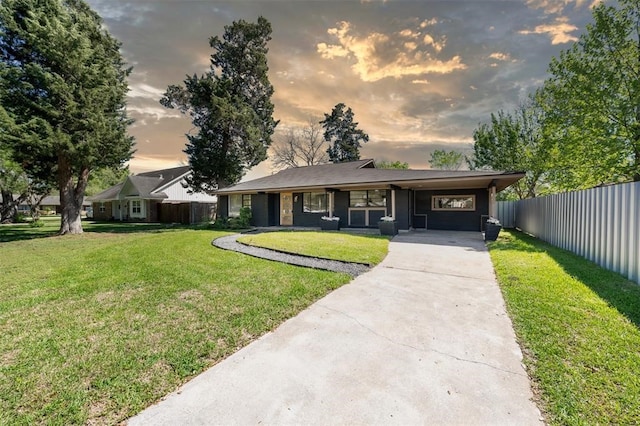 view of front facade with driveway, fence, an attached carport, and a yard