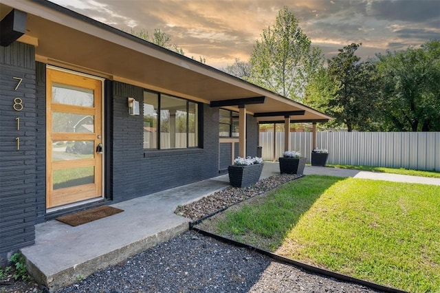 property exterior at dusk featuring a yard, brick siding, and fence