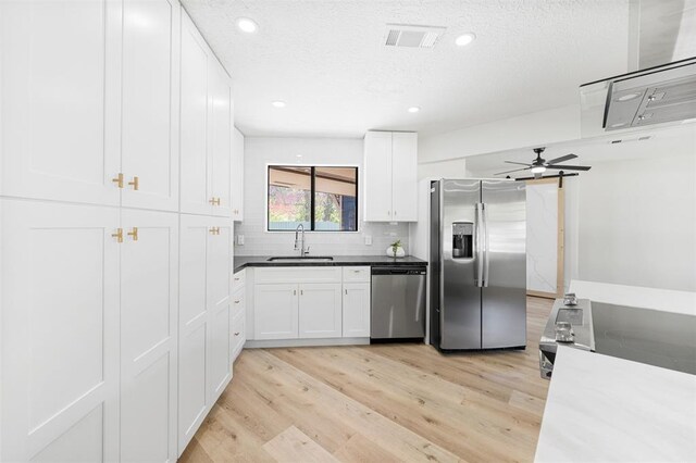 kitchen with backsplash, appliances with stainless steel finishes, light wood-style floors, white cabinets, and a sink