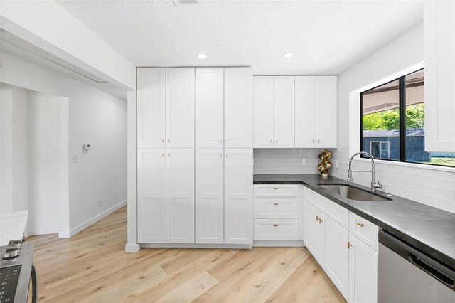 kitchen with light wood finished floors, white cabinets, dishwasher, dark countertops, and a sink