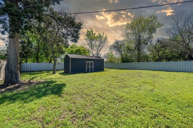 yard at dusk with an outbuilding, a fenced backyard, and a storage unit