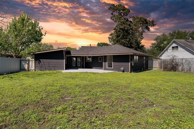 back of house at dusk featuring a fenced backyard, a lawn, and a patio