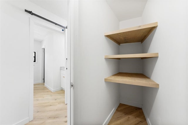 hall with light wood finished floors, a barn door, and baseboards