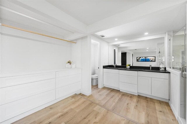 bathroom with a stall shower, toilet, beamed ceiling, wood finished floors, and vanity