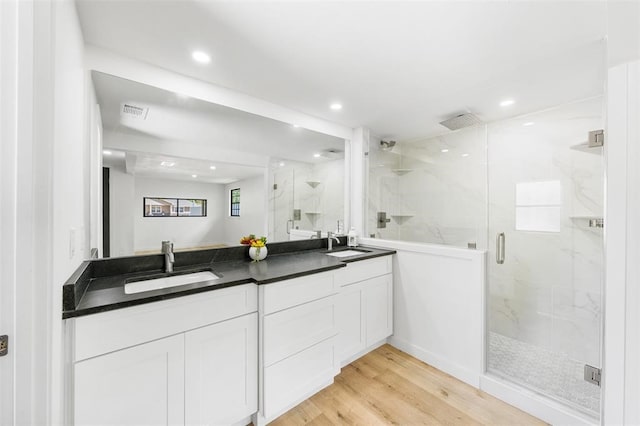 bathroom featuring double vanity, a sink, a marble finish shower, and wood finished floors