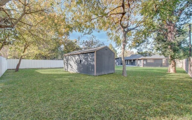 view of yard with a fenced backyard, an outdoor structure, and a storage unit