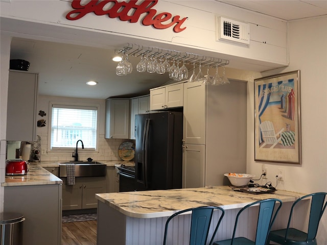 kitchen with tasteful backsplash, visible vents, freestanding refrigerator, a sink, and a peninsula