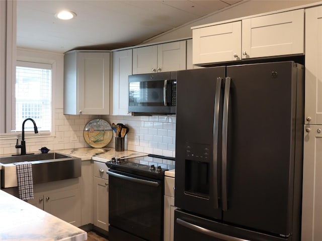 kitchen featuring lofted ceiling, light countertops, decorative backsplash, a sink, and black appliances