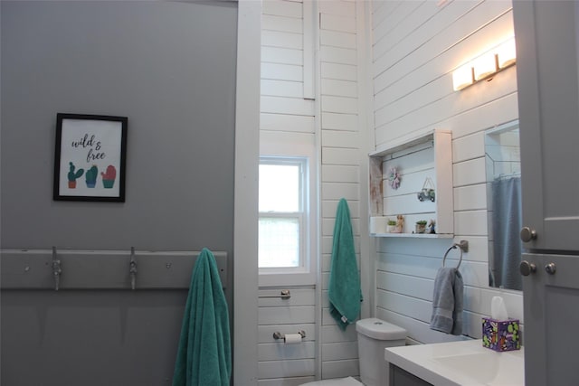 bathroom with toilet, wooden walls, a towering ceiling, and vanity