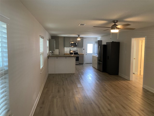 kitchen with a peninsula, wood finished floors, baseboards, appliances with stainless steel finishes, and decorative backsplash