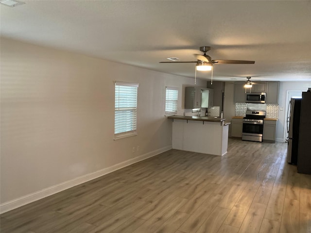 kitchen featuring baseboards, decorative backsplash, appliances with stainless steel finishes, wood finished floors, and a peninsula